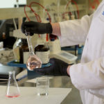 An employee holds a beaker of liquid at Nephron in the Central SC Region