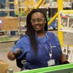 A female employee smiling while handling machinery inside a Samsung facility in Central SC