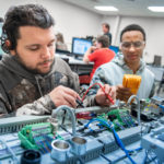 Two male students work on a manufacturing device at Piedmont Tech in the Central SC Region