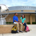 Two students sit on the edge of a fountain outside of a building on the Central Carolina Technical College in the Central SC Region