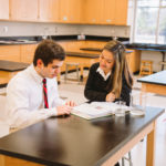 Two students sit side by side while reviewing a textbook at Cardinal Newman in the Central SC Region