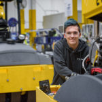 A young male employee smiles while working on a construction vehicle at BOMAG in the Central SC Region
