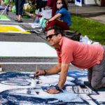 A man smiles while painting a mural on the street during the West Columbia and Cayce Art Festival in Central SC